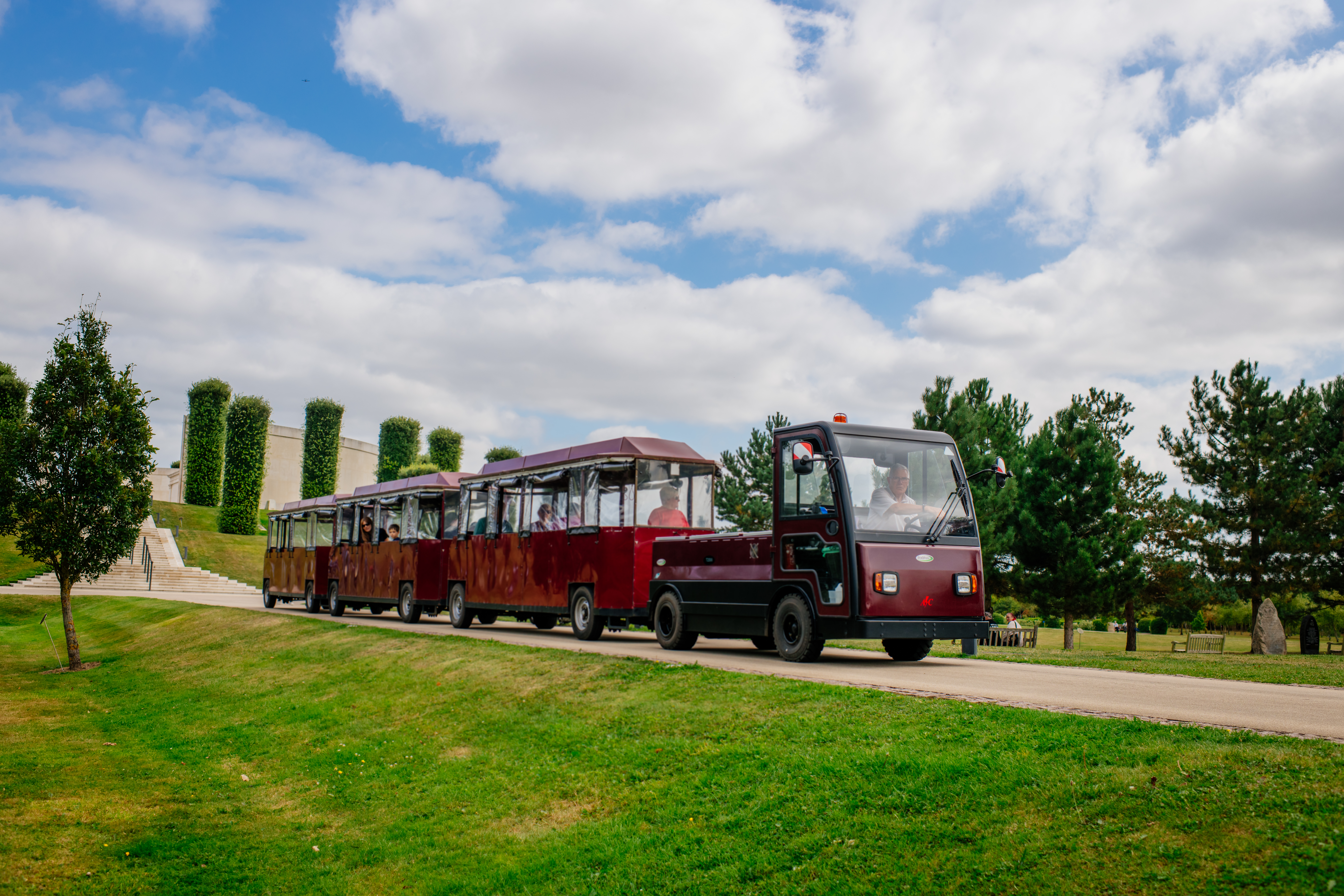 Land Train driving down a pathway with the Armed Forces memorial in the rear