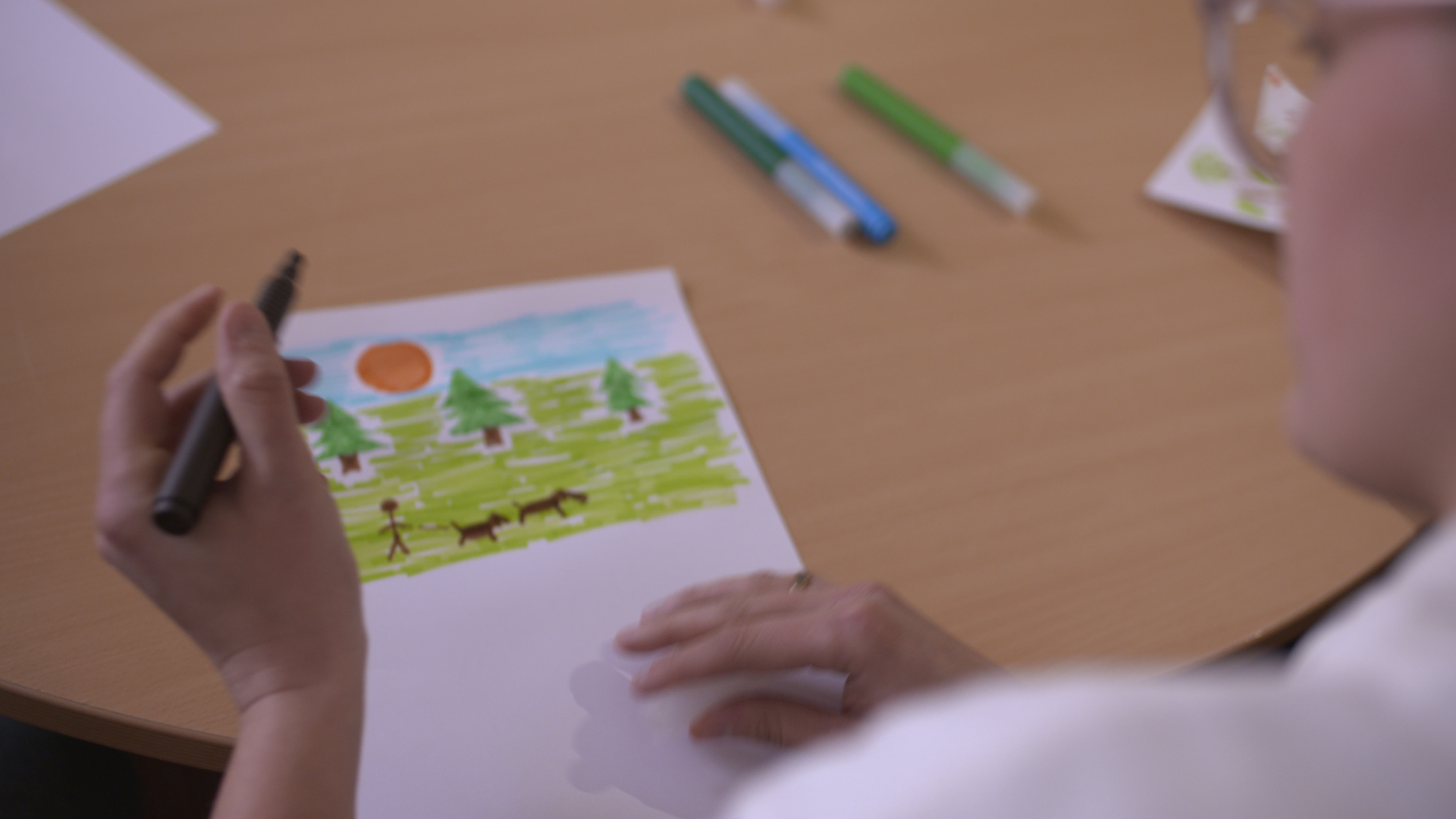 A person taking part in the workshops, colouring in an image of a dog walker in a park.
