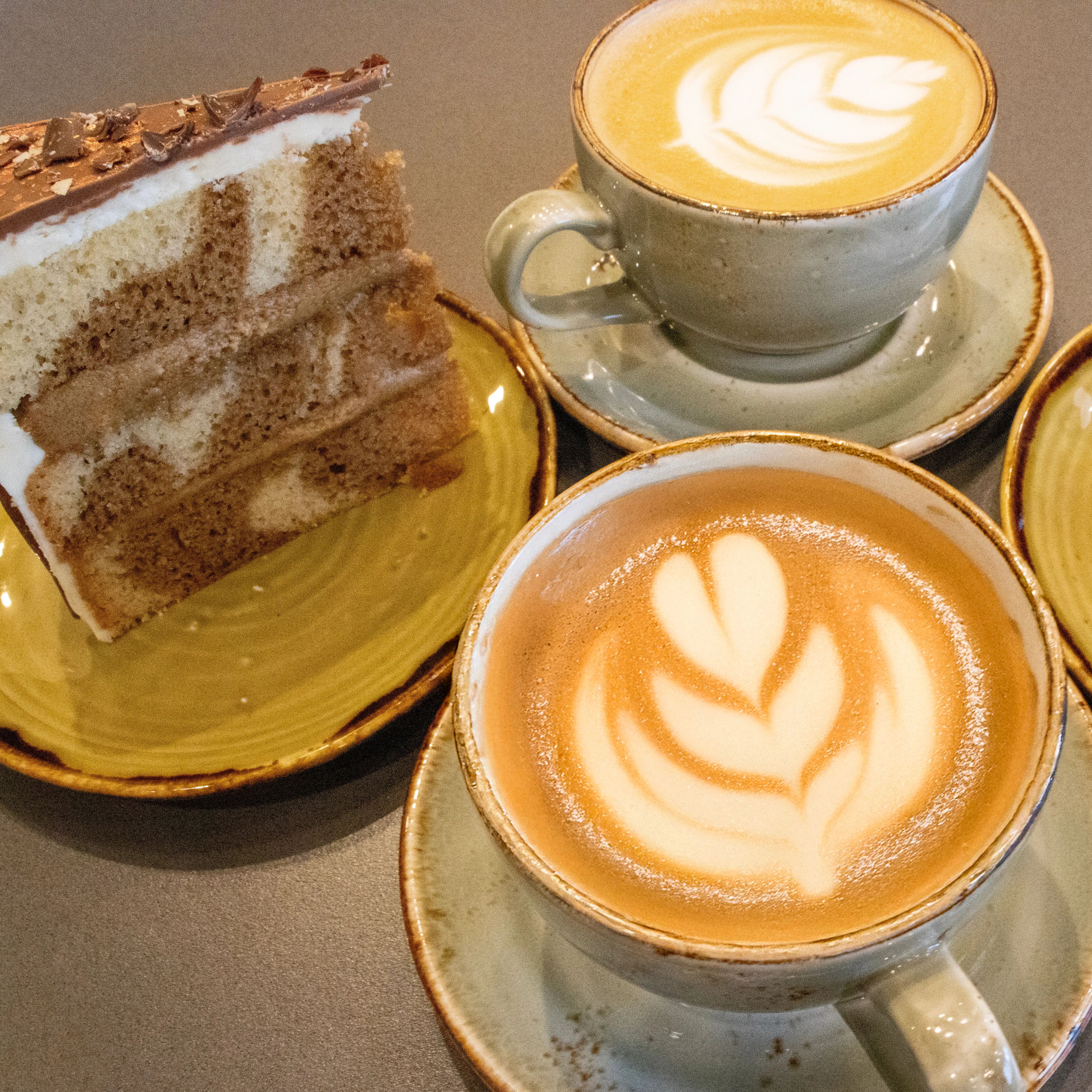 Barista fresh coffees in mugs at the coffee shop, next to a slice of cake.