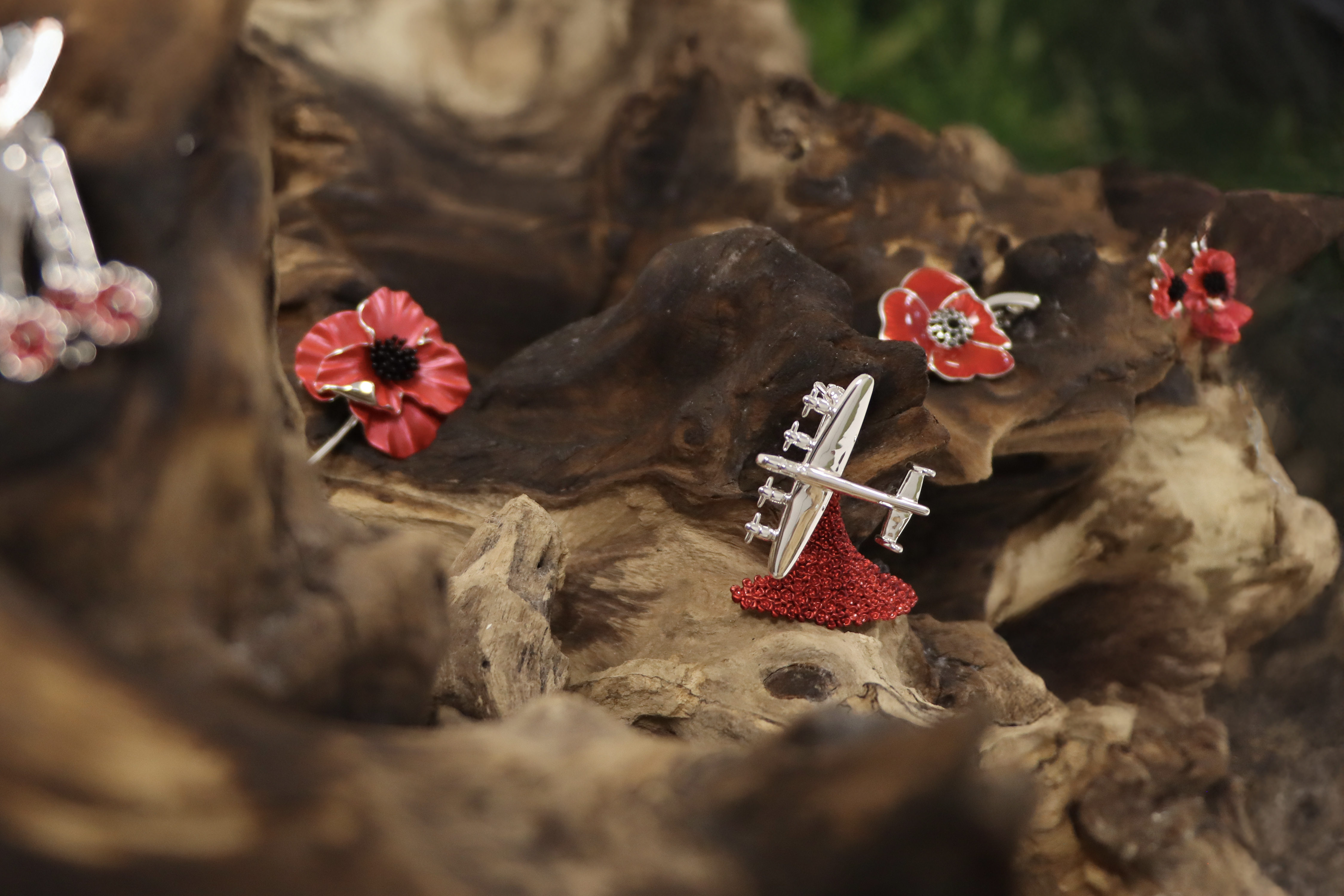 Red poppy brooches and earrings sit upon a wooden log display stand