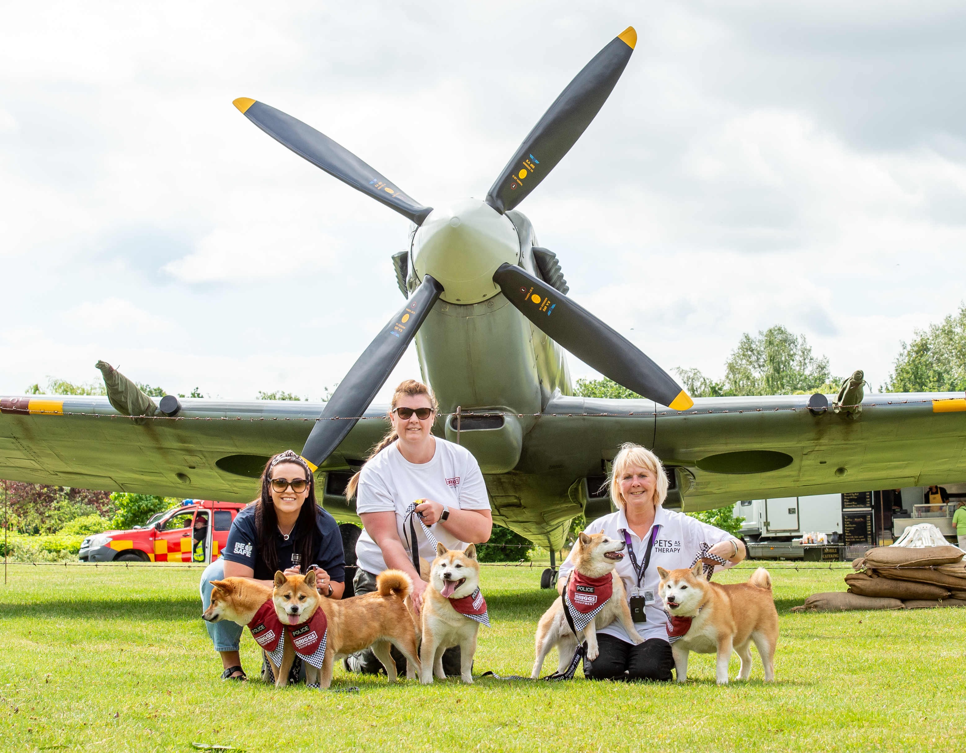 Briggs equipment staff members posing with therapy dogs in front of an aeroplane during Armed Forces Weekend event.