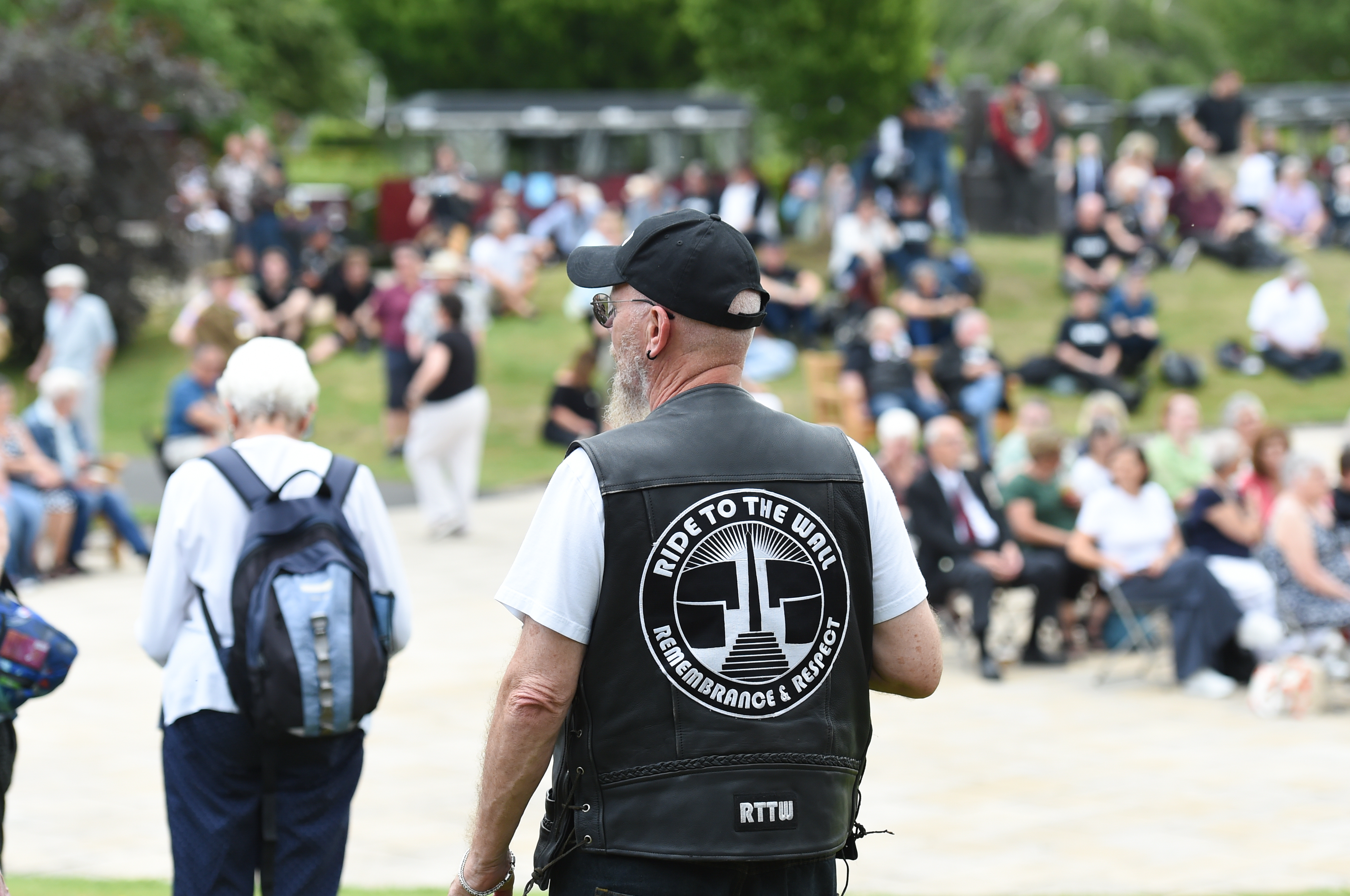A man wearing a Ride to the Wall jacket stood looking at a crowd of people at the Arboretum