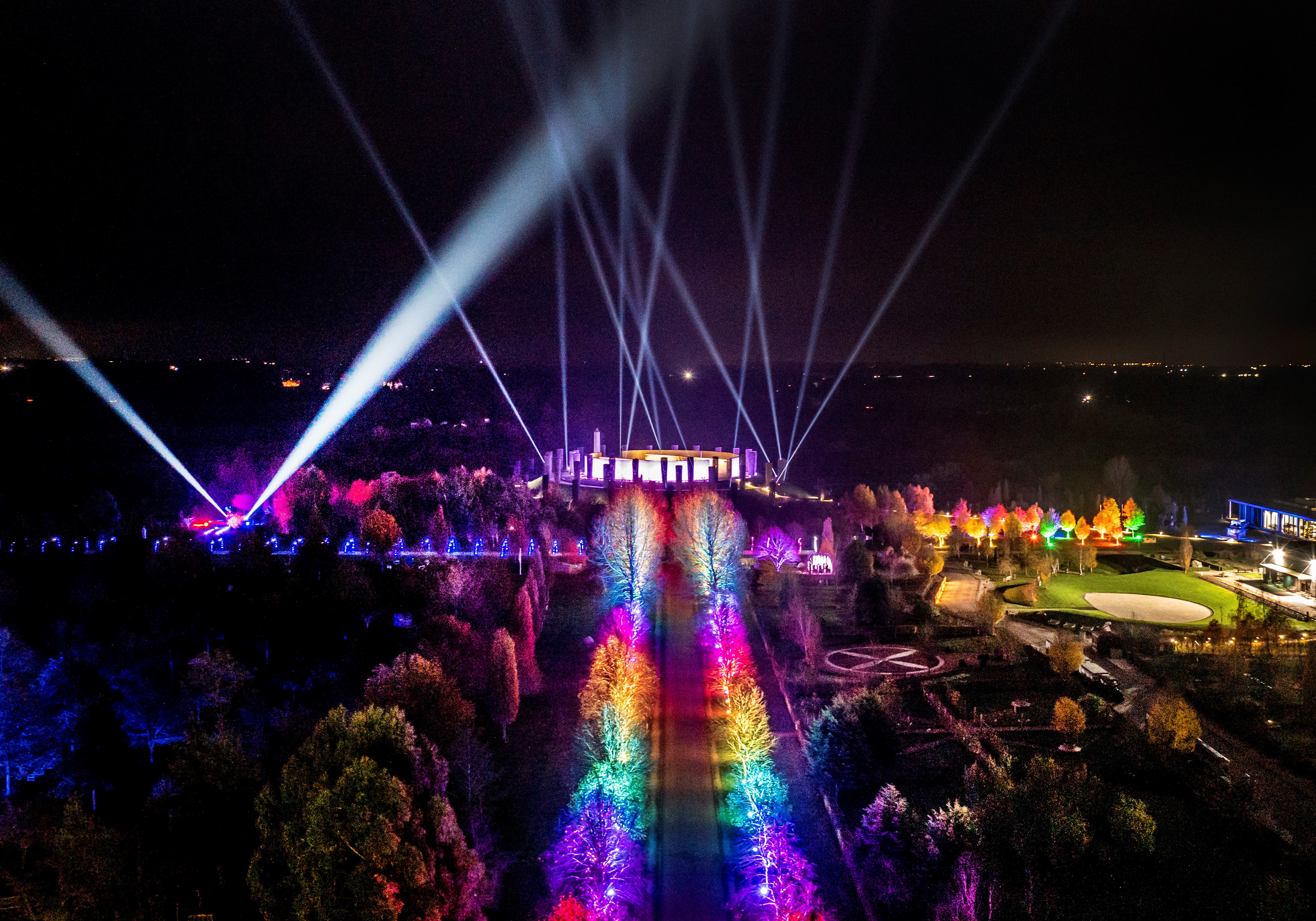 A drone image of the Armed forces memorial lit in a rainbow of light. The sky is dark.