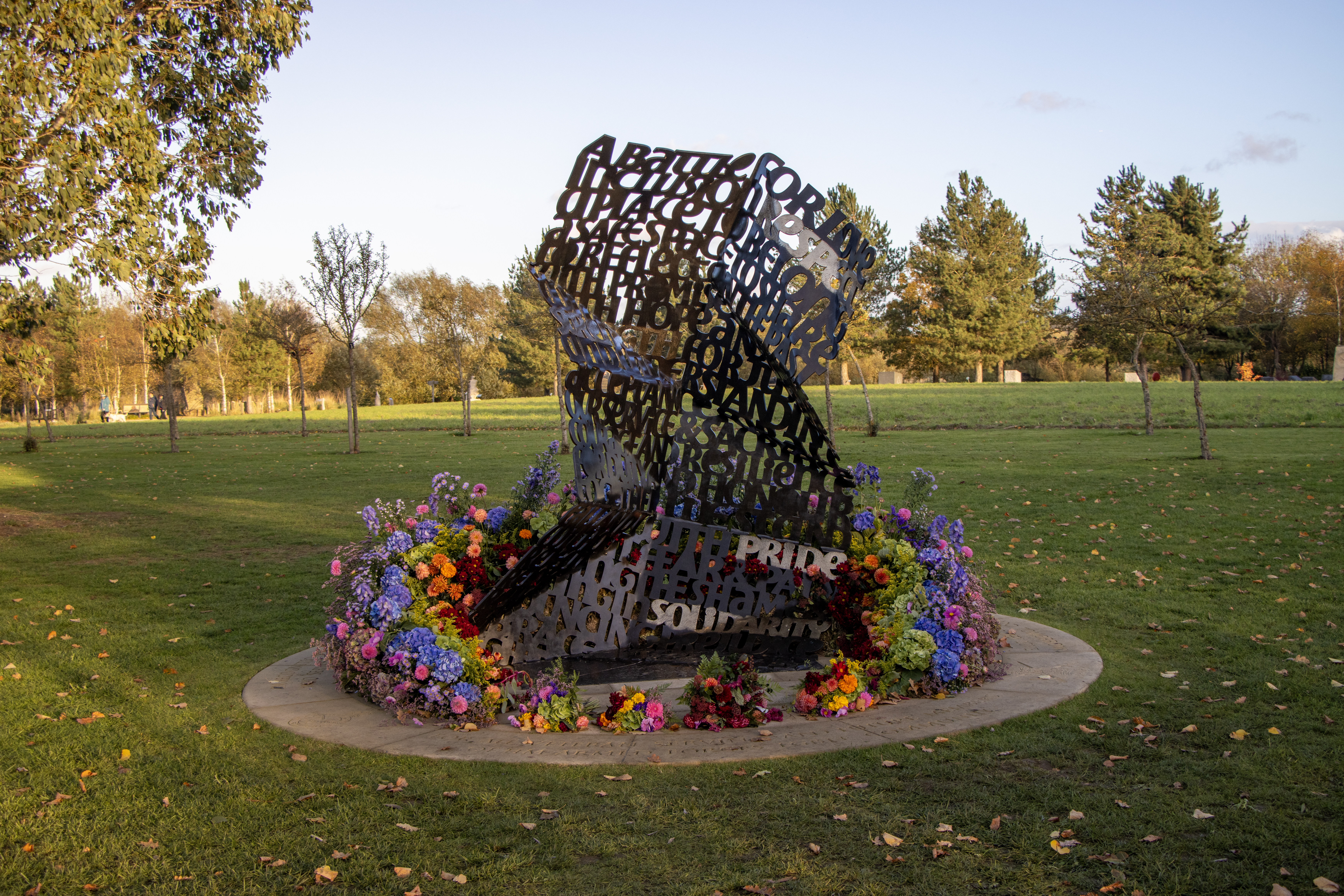 The LGBT Armed Forces Community Memorial on dedication day, surrounded by multicoloured floral arrangements