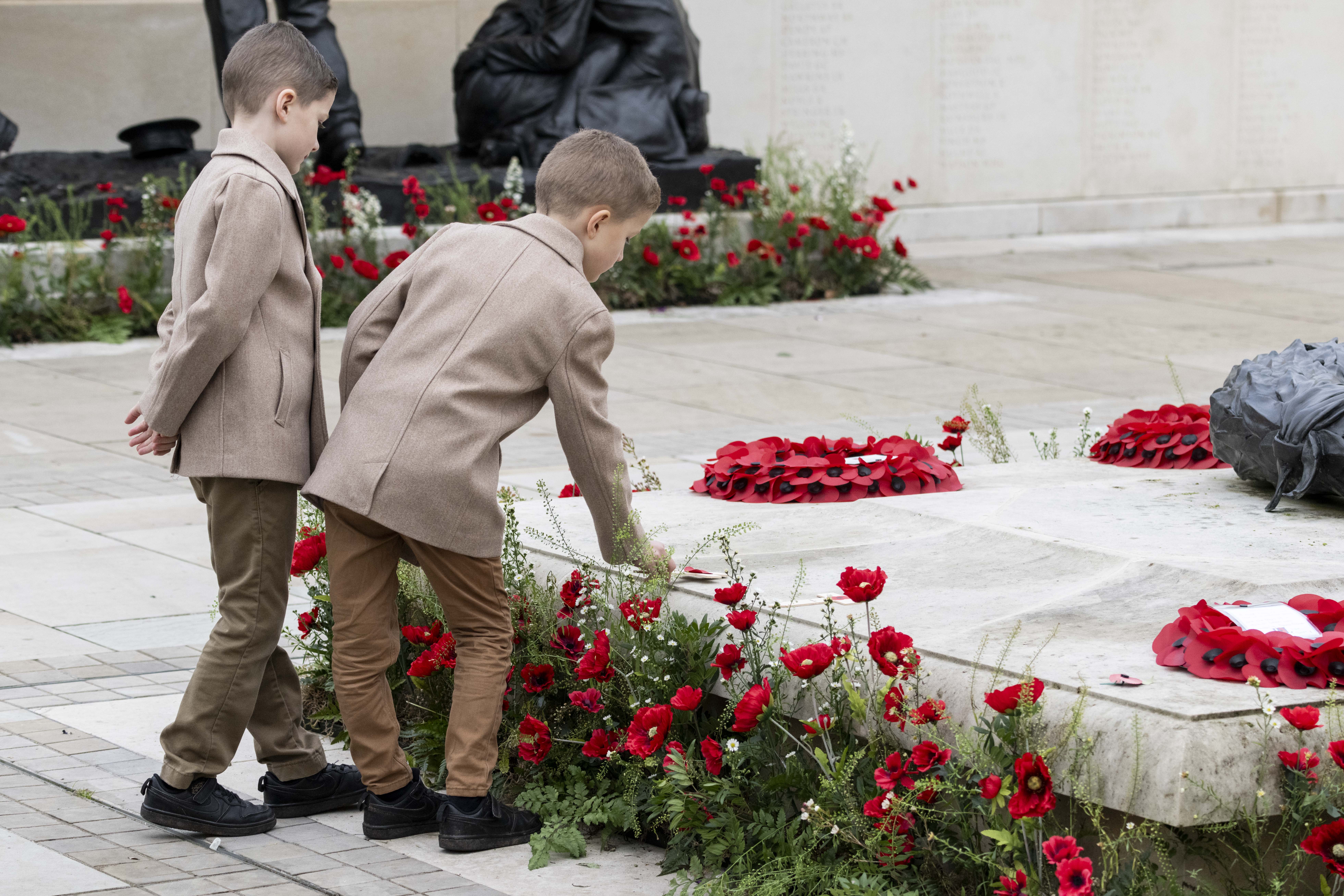 Two young boys dress identically in wool coats lay a poppy tribute onto the central wreath on the Armed Forces Memorial.
