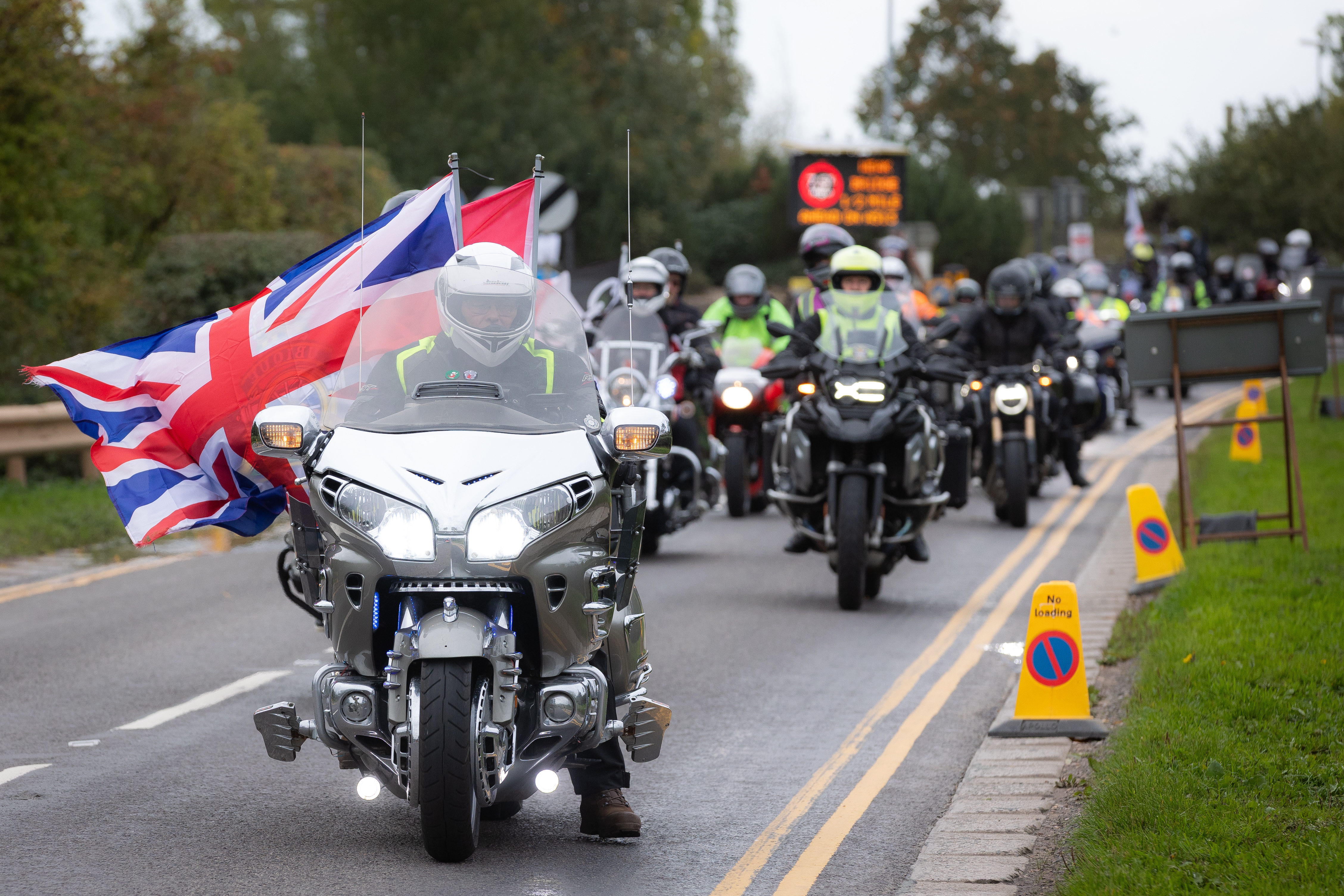 A silver motorcycle carrying a Union Jack flag rides along Croxall Road towards the Arboretum, followed by hundreds of other bikers.