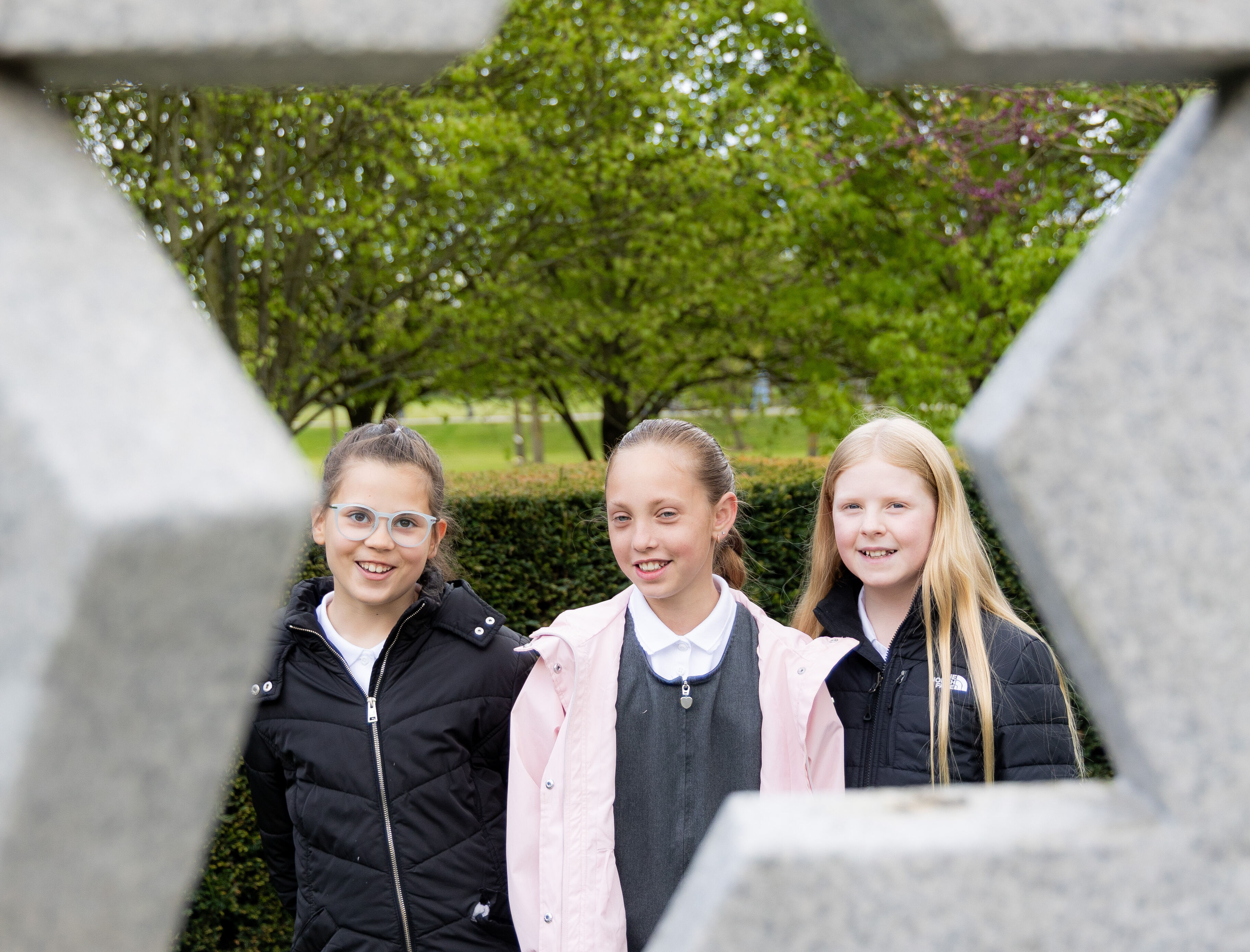 Key Stage Two students visiting the Association of Jewish Ex-Servicemen and Women Memorial. They are smiling and looking at the memorial's star design.