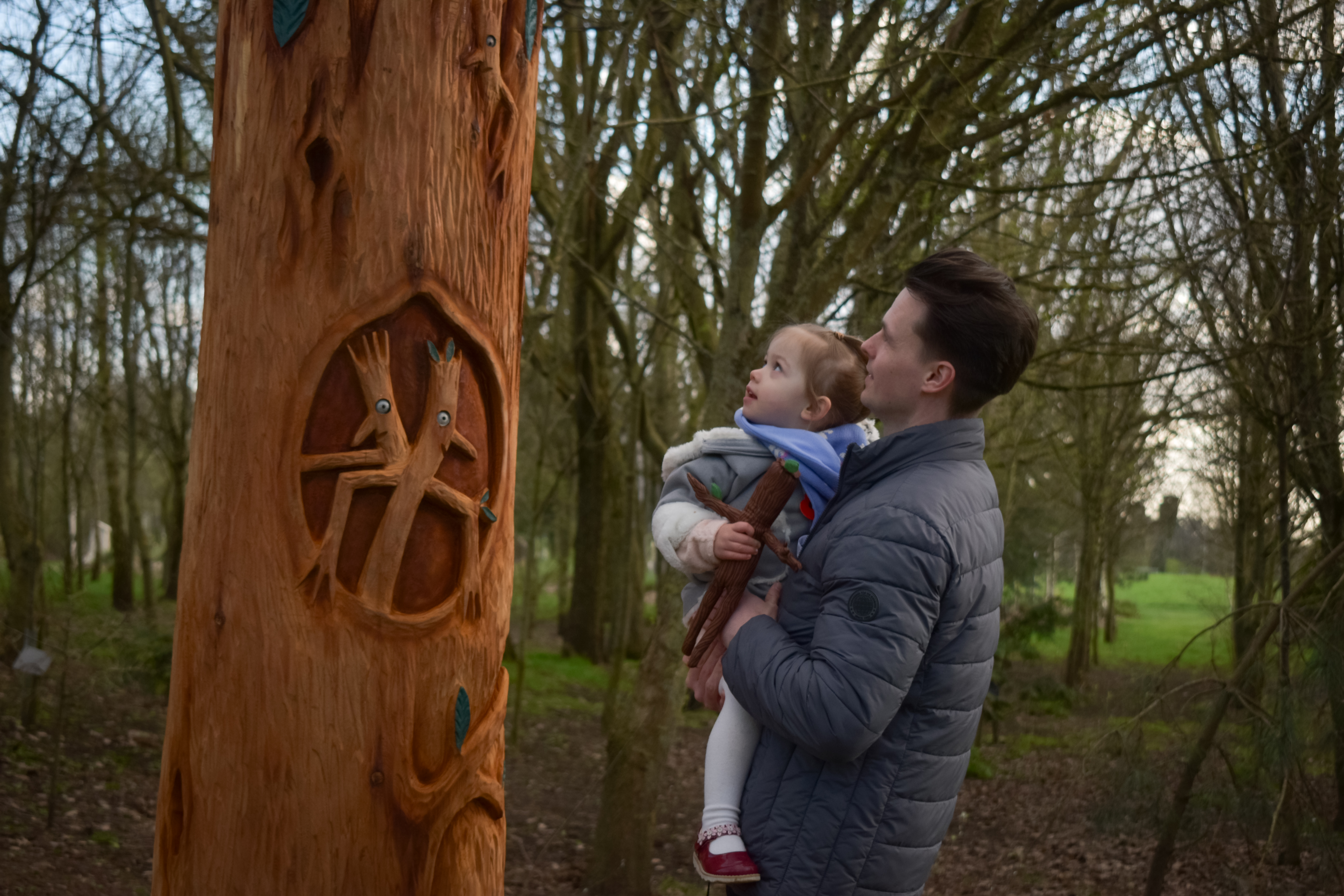 A man holding his daughter to look at the sculptures along the Stick Man trail at the National Remembrance Gardens
