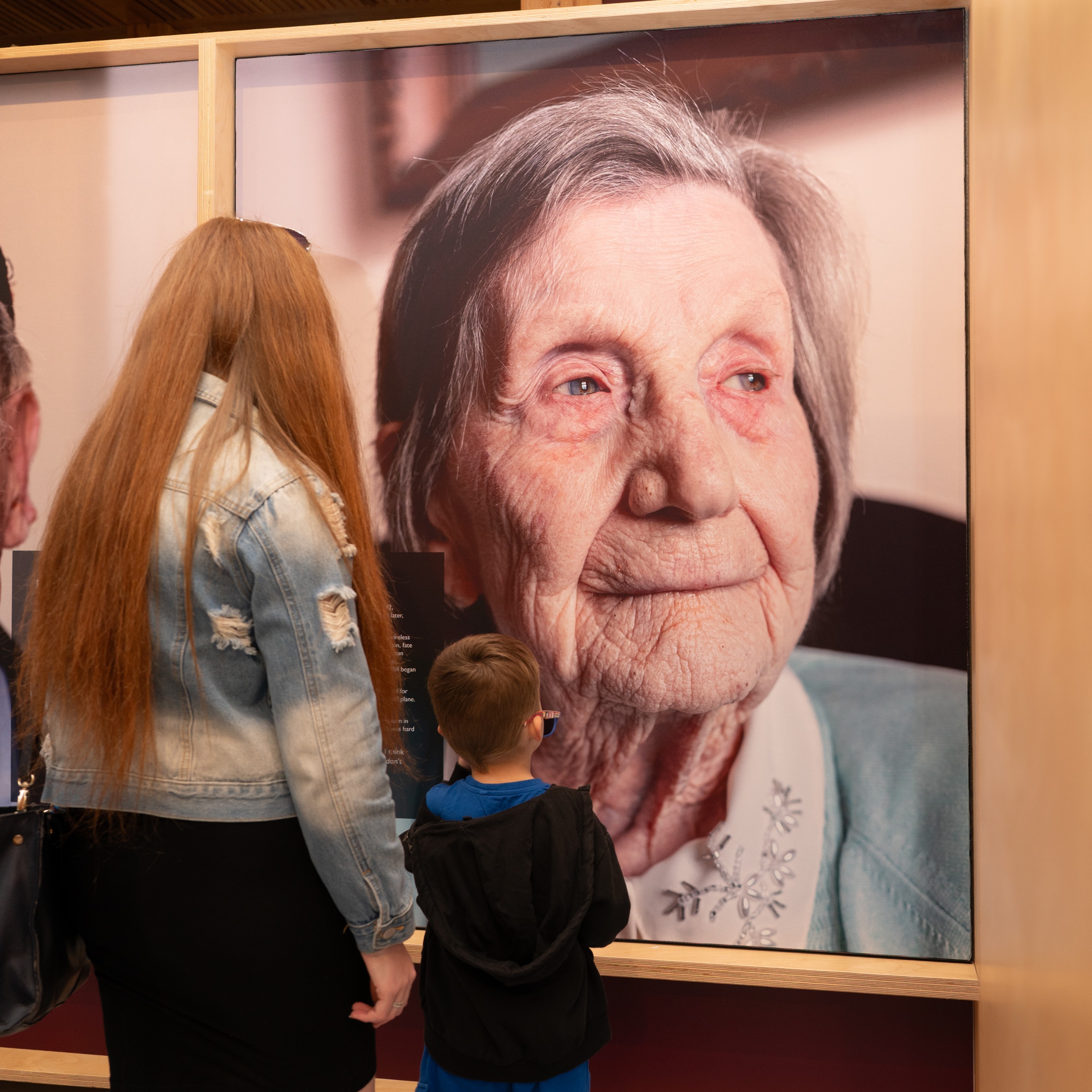 A woman and young boy looking at a portrait of a WWII veteran featured in the indoor exhibition.