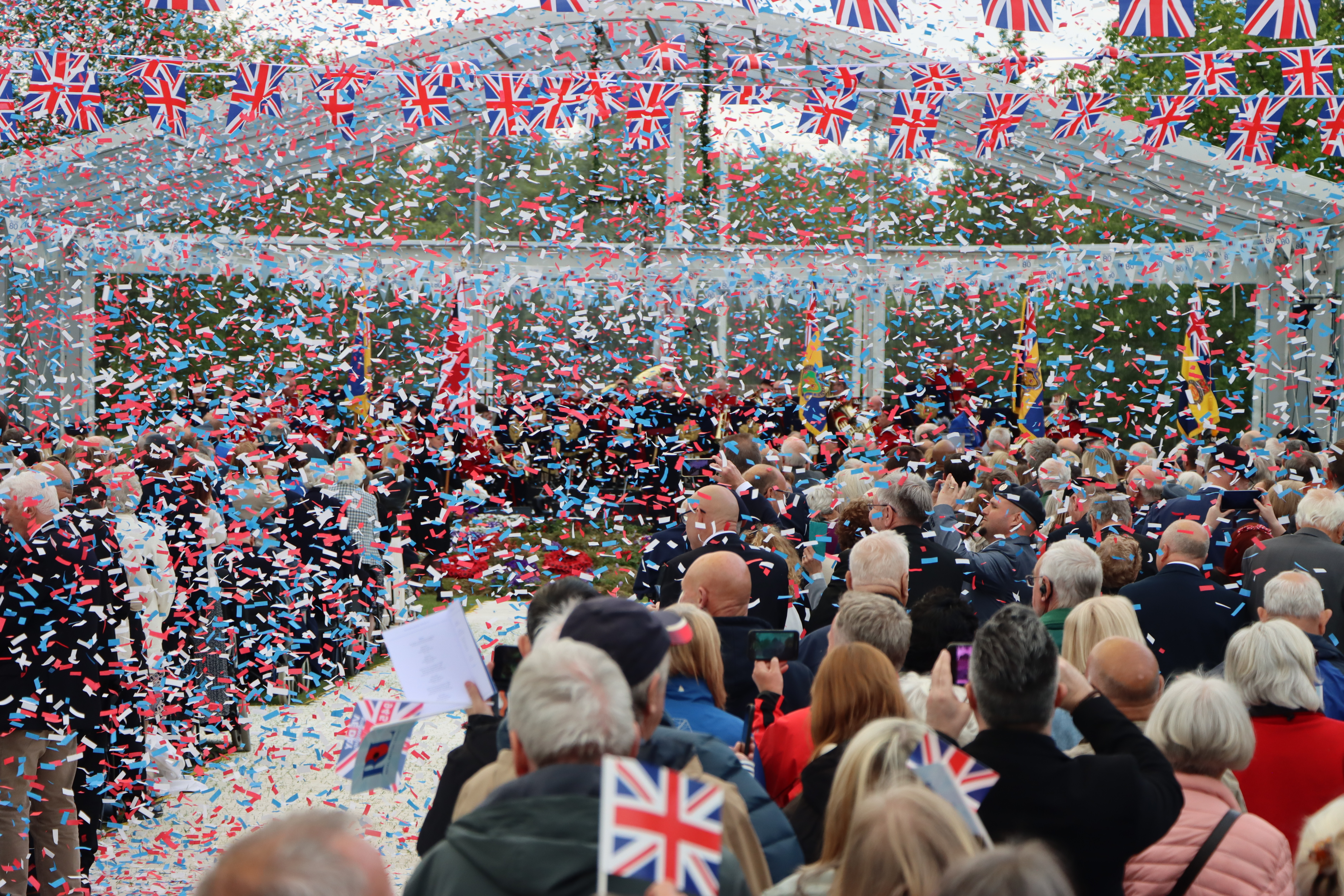 A crowd surrounding by falling paper bunting watch the VE Day 80 Remembrance
