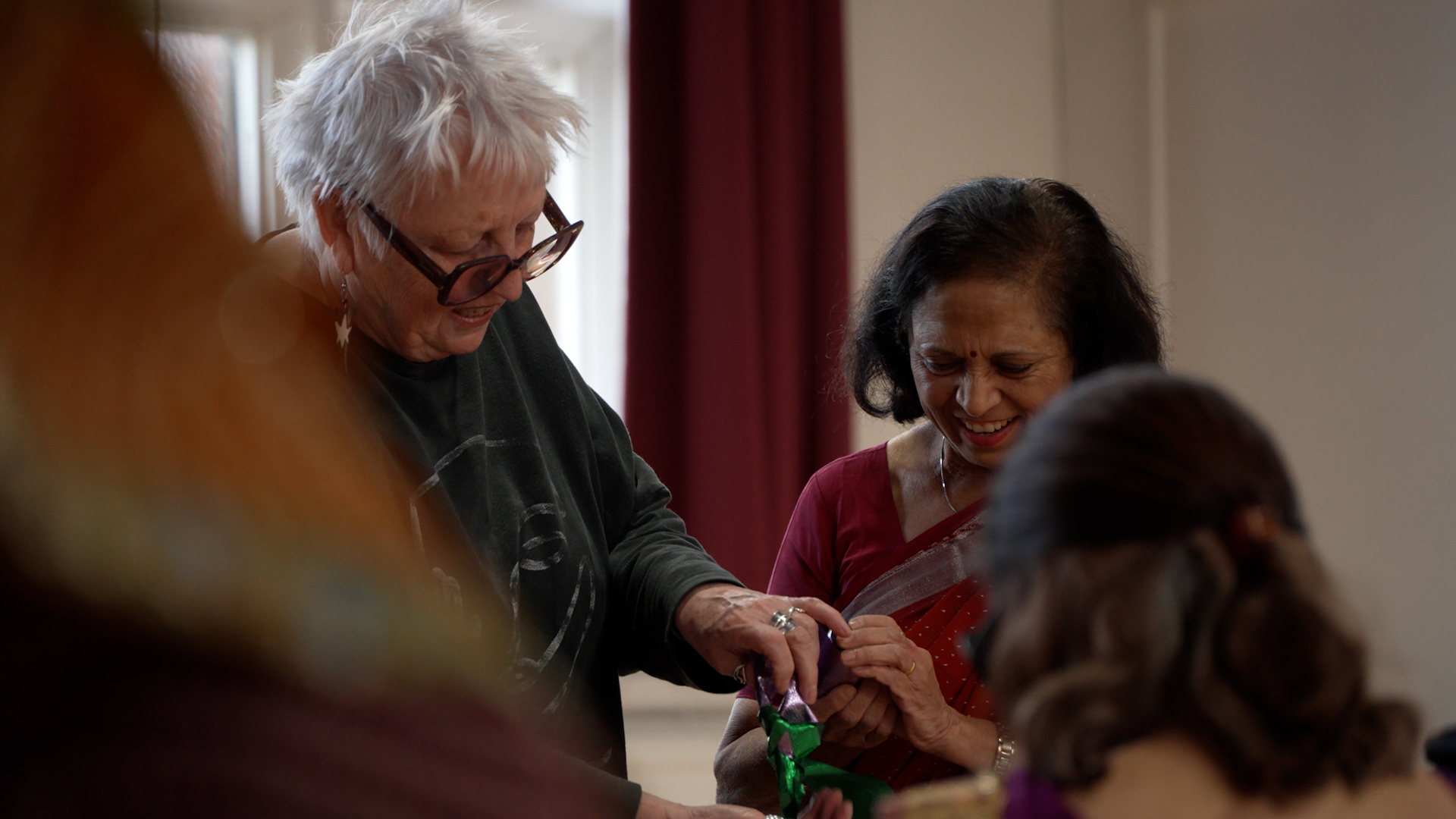 Two women laugh together while holding shiny crafting materials.