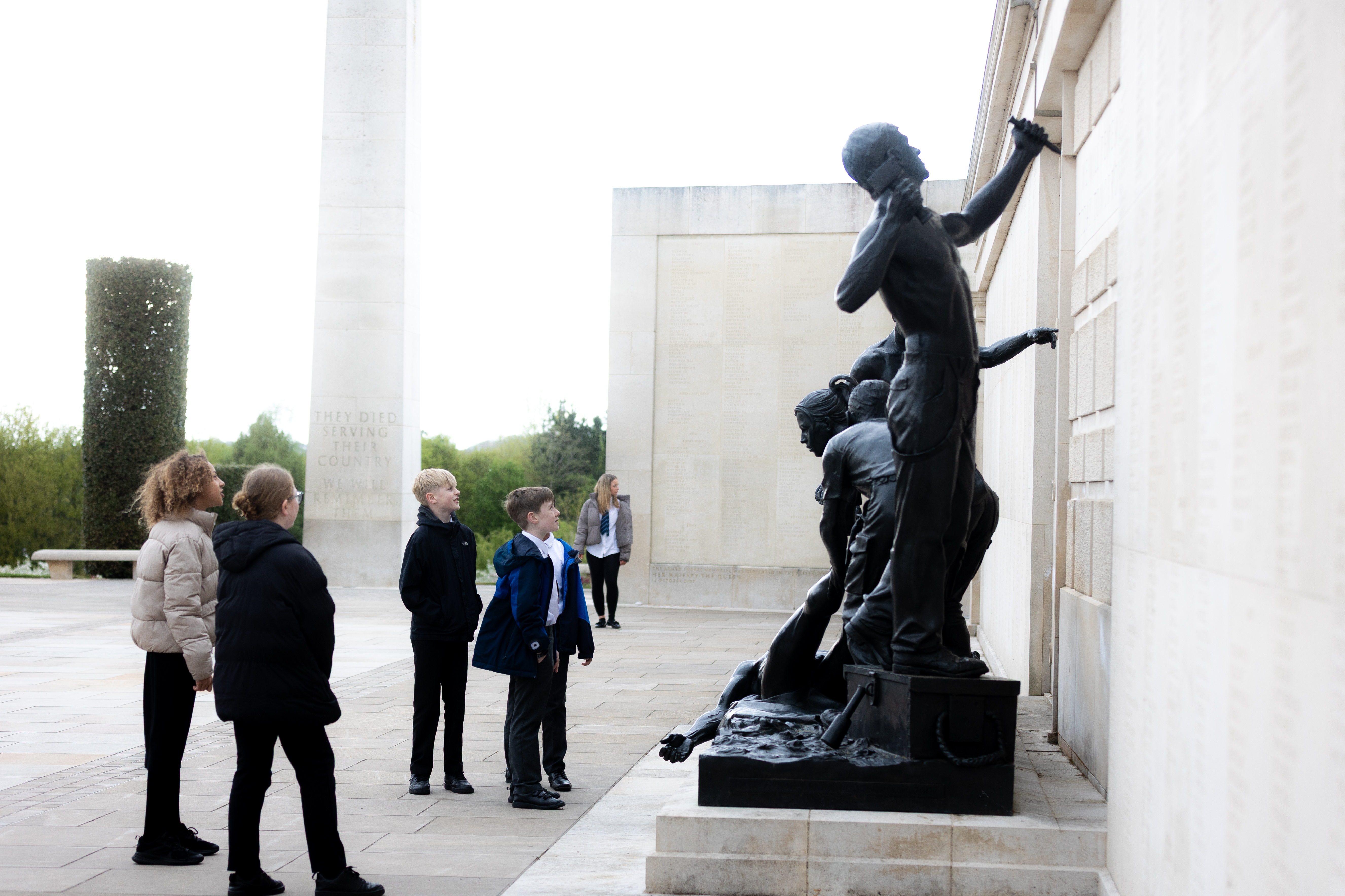 Secondary school children looking at the sculptures on top of the armed forces memorial