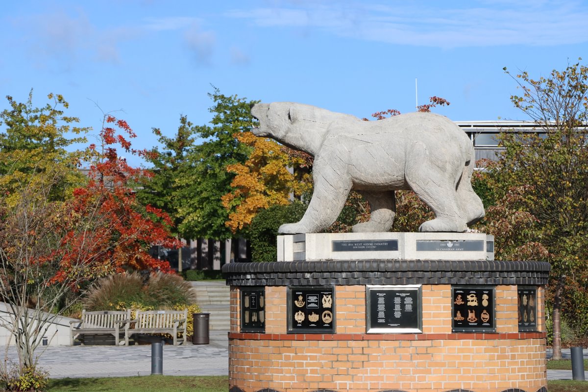 Wooden polar bear on a raised brick platform surrounded by autumn trees with a clear blue sky