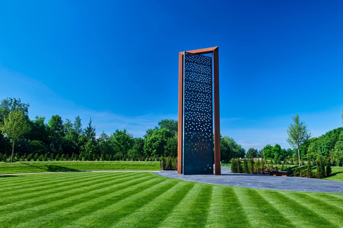 12 metre high brass pannel with leaf shaped apertures surrounded by green grass and a clear blue sky