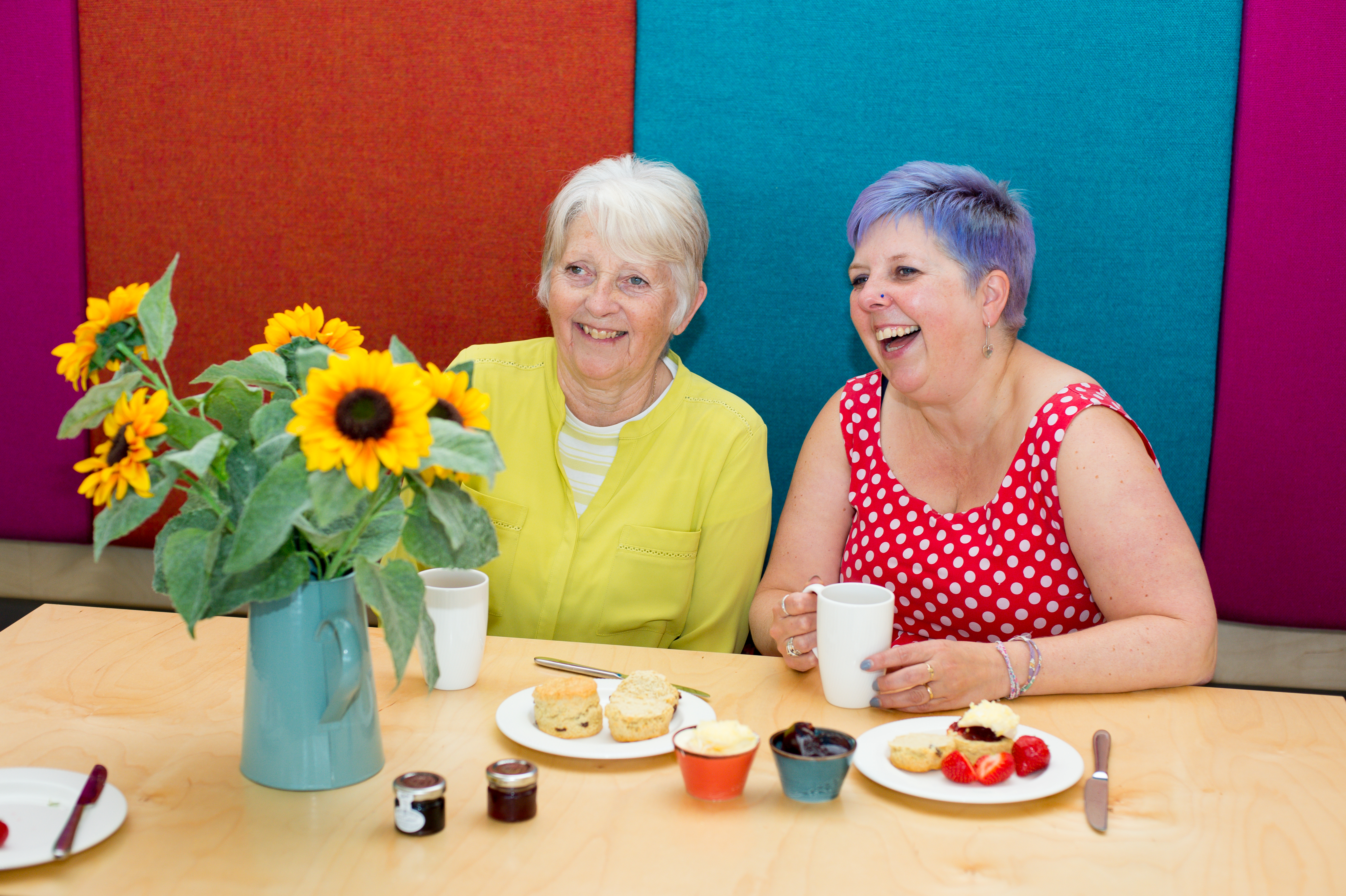 Ladies sit on colourful seats drinking coffee and smiling 