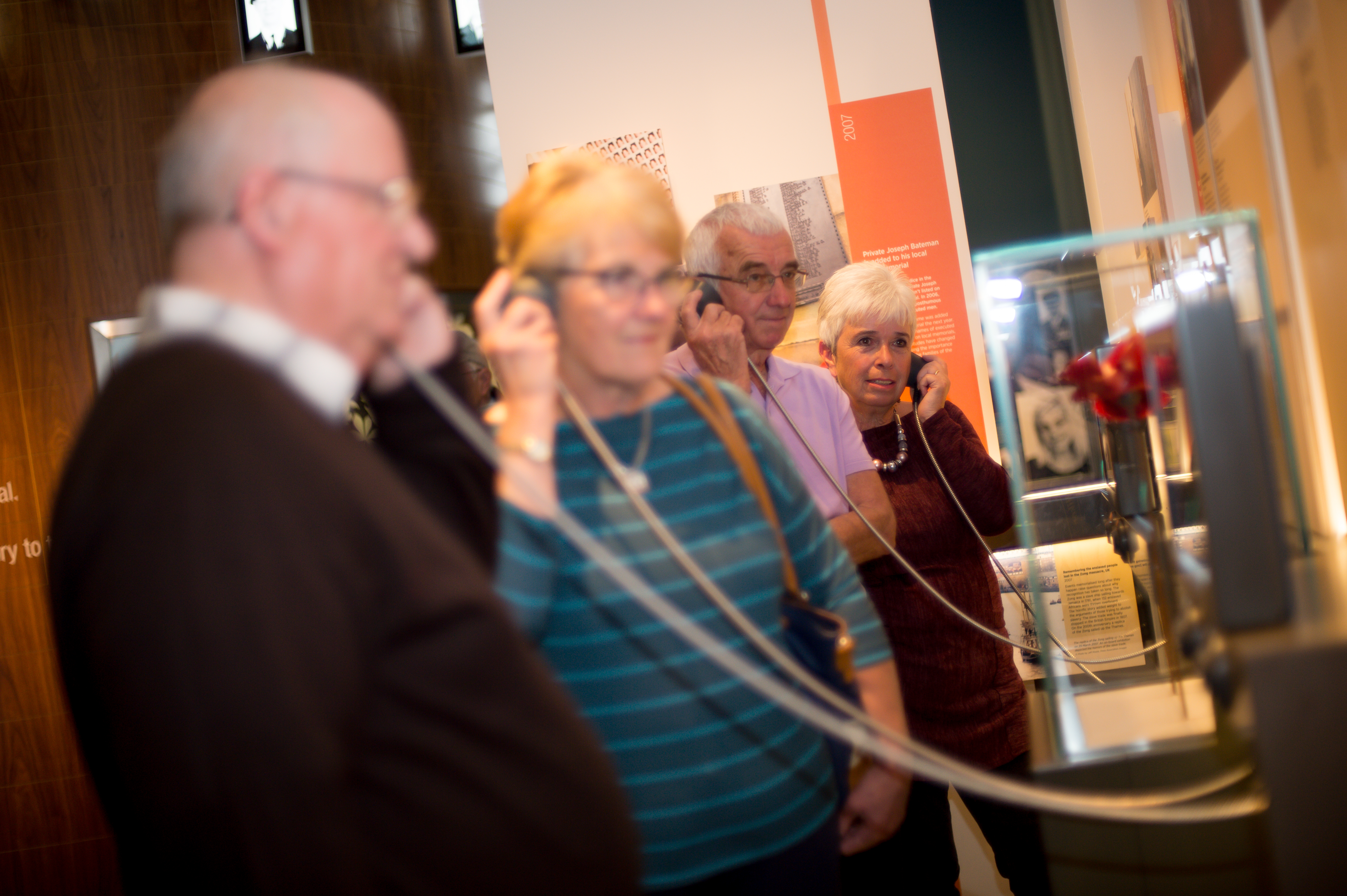 Visitors in the Landscapes of Life exhibition, listening to one of the displays on chorded speakers held to their ears.
