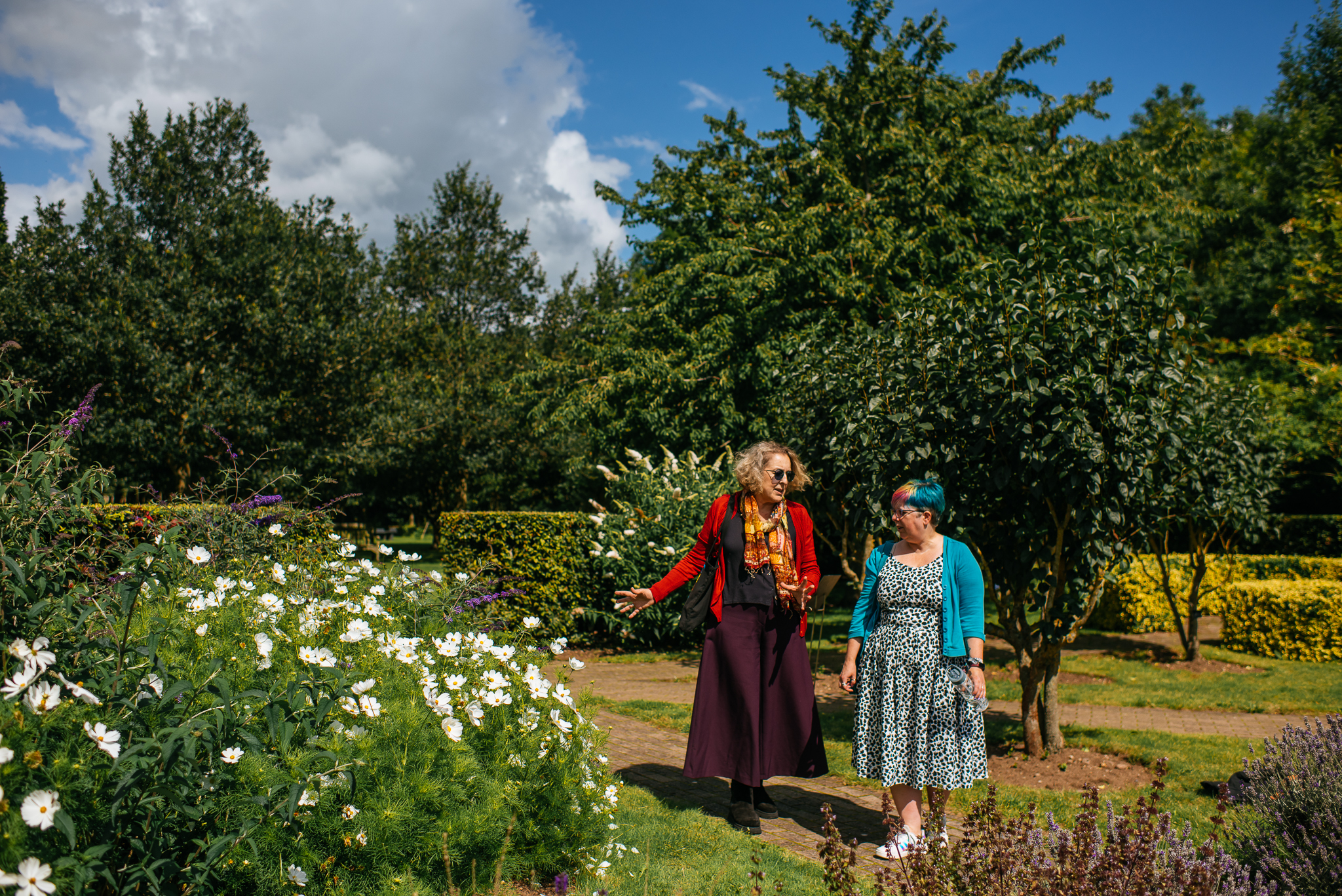 Two female visitors exploring the gardens, looking at white flowers while engaged in conversation.