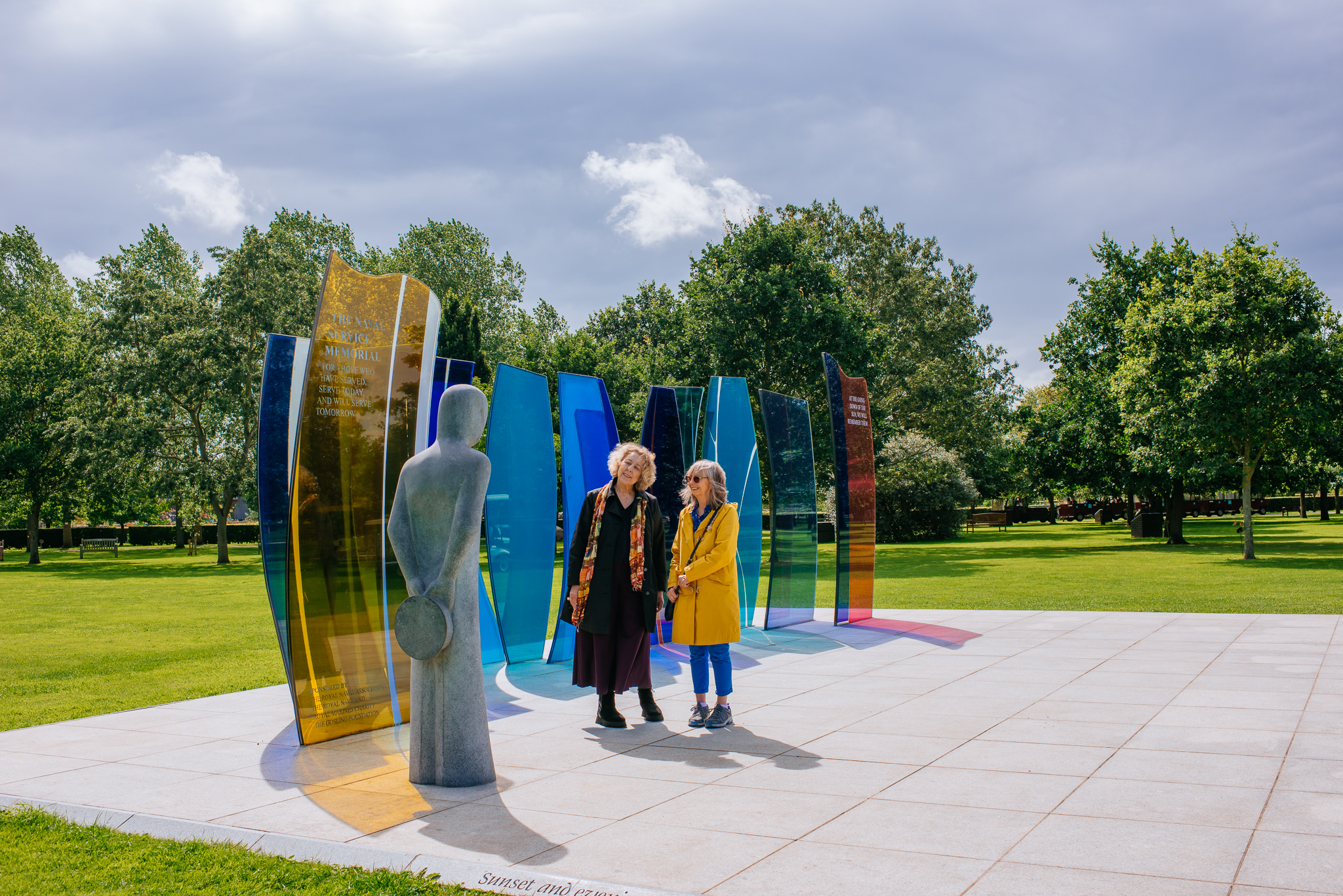 Two female visitors at the Naval Services Memorial, looking up at a large stone sailor sculpture.