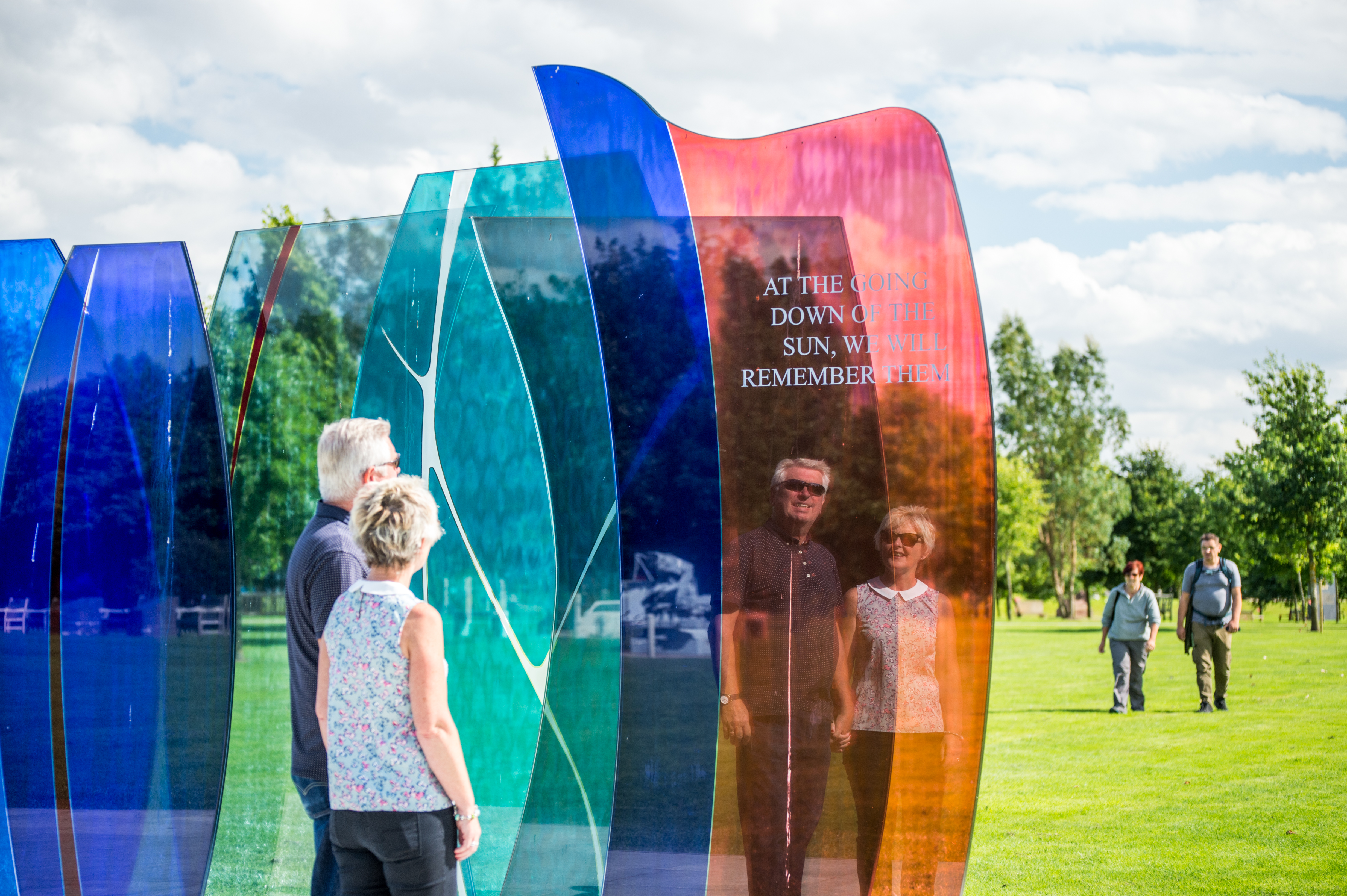 Two visitors looking at the Naval Services Memorial. They appear to be a couple. It is a sunny day, and both are in short sleeves and wearing sunglasses.