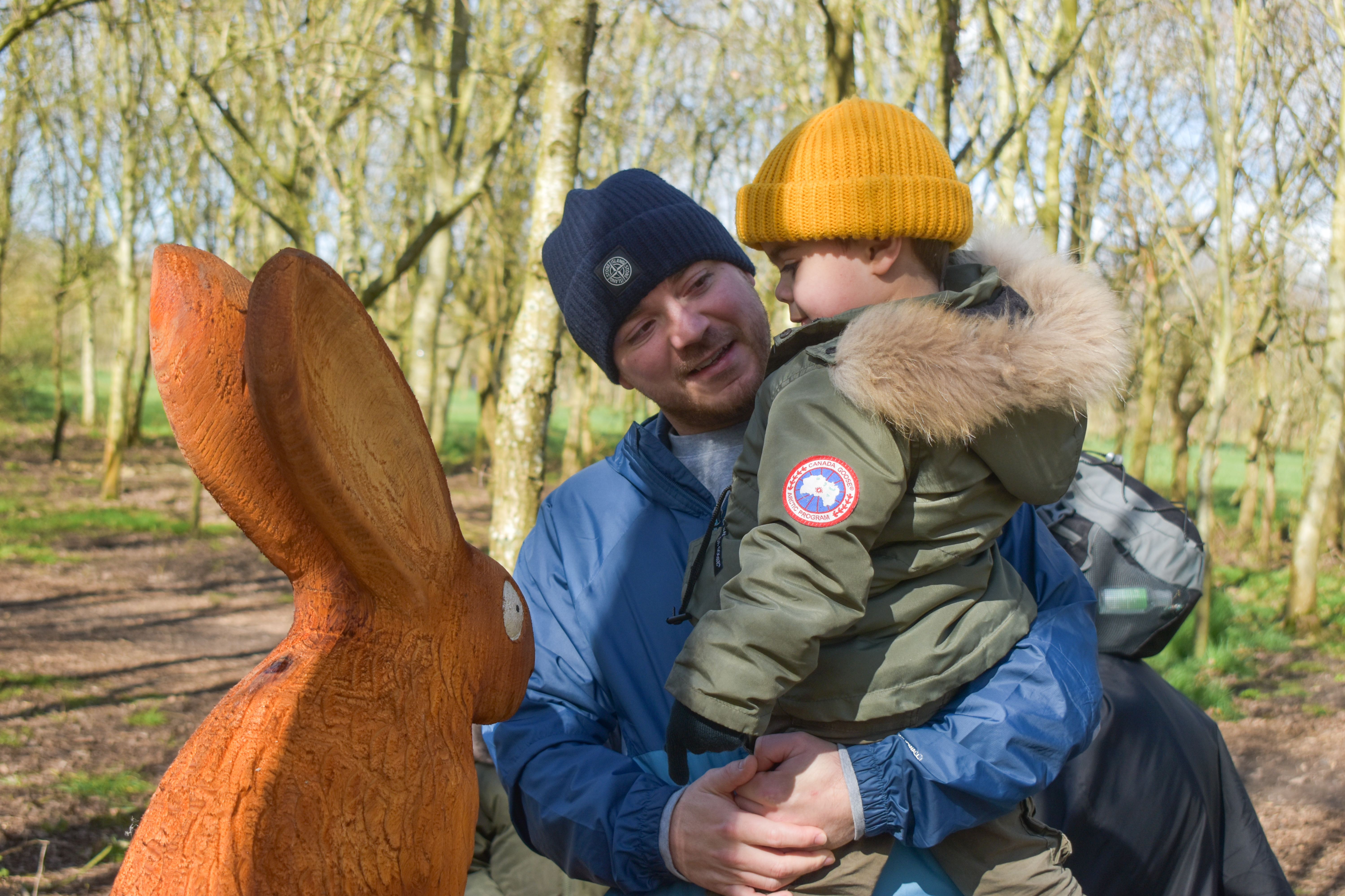 A young boy and a man look at a rabbit carving, both are wearing colourful hats