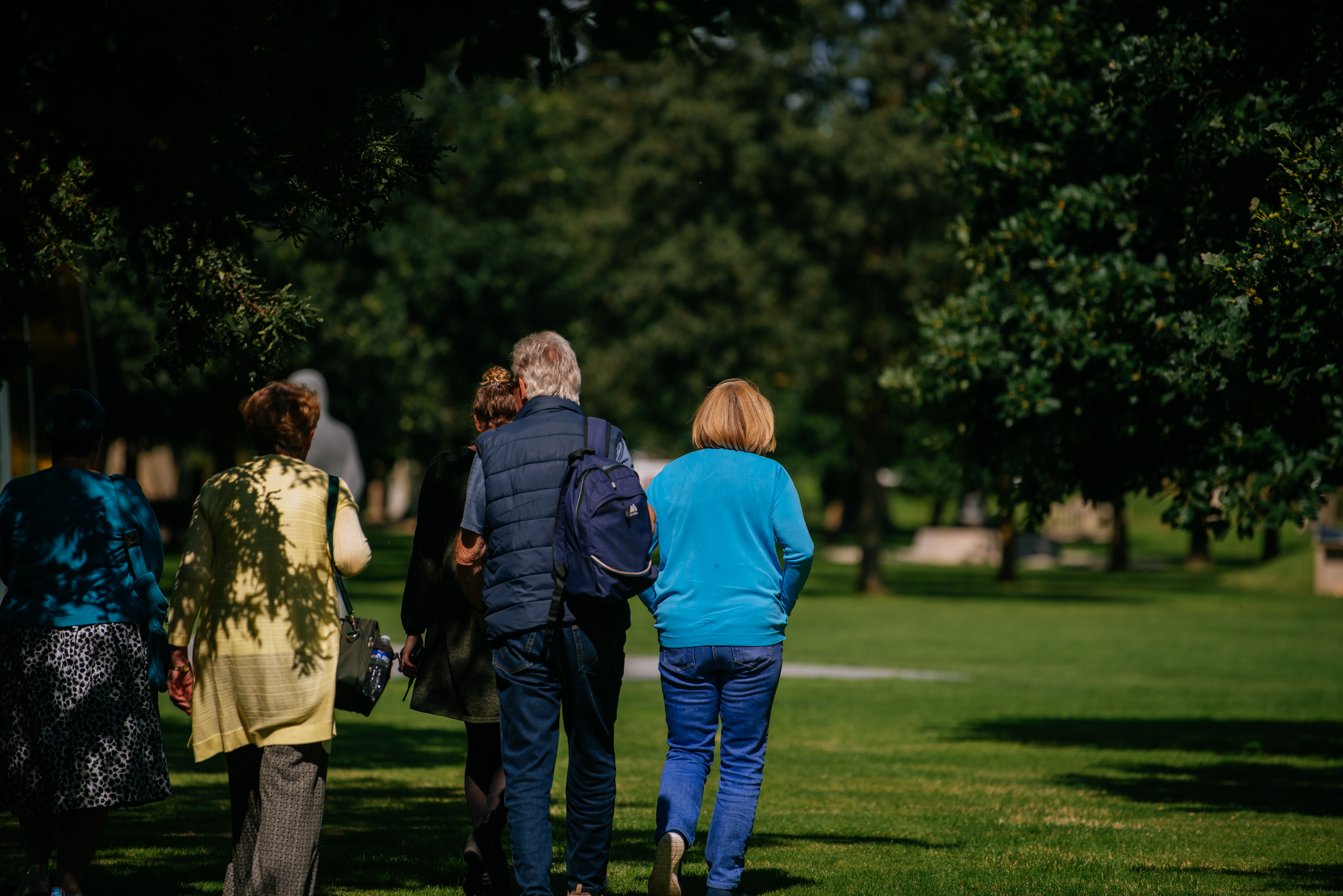 Visitors walking through the grounds, away from the camera. It is a sunny day, and the grass and trees are a rich green.